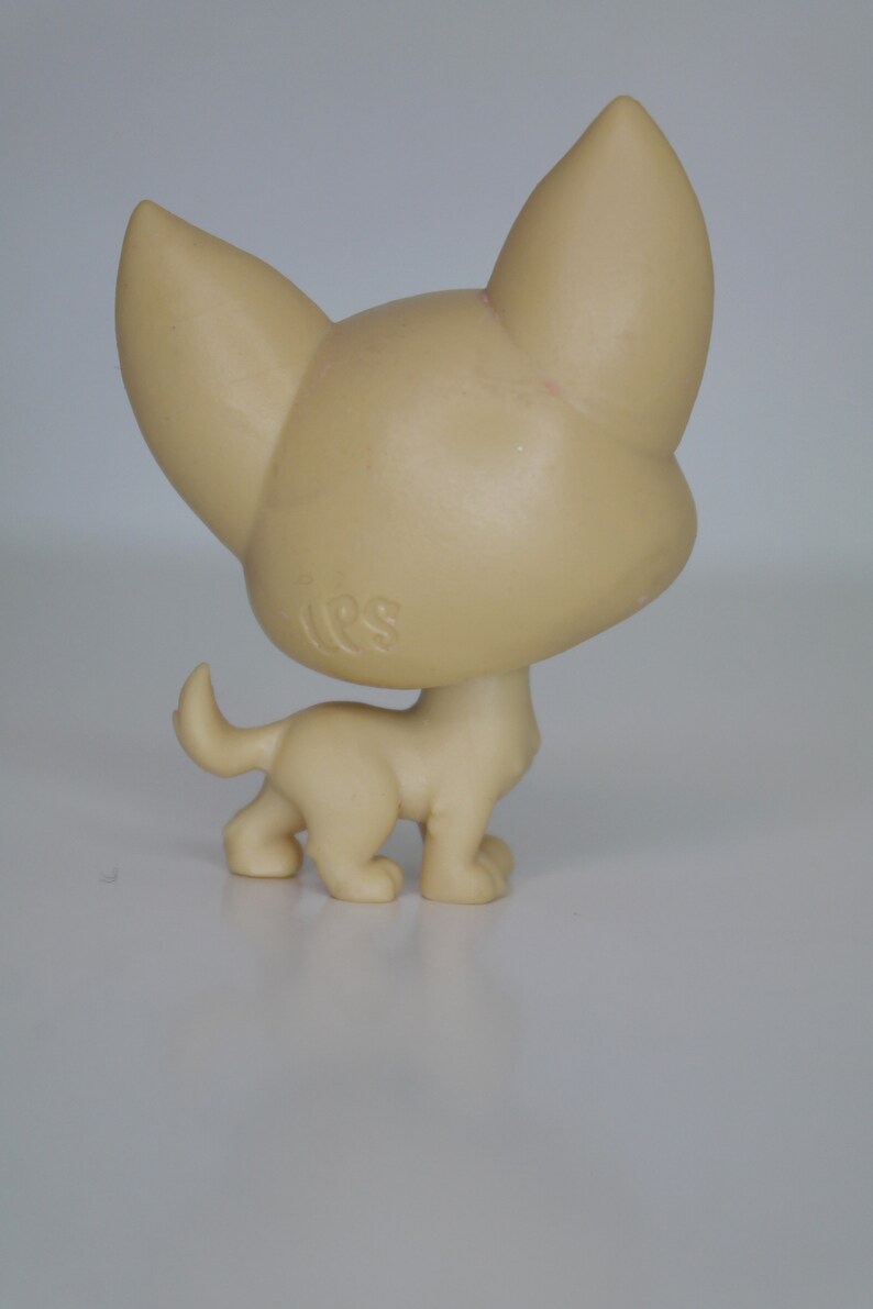 May include: A small, beige plastic toy dog with floppy ears and a short tail. The dog is standing on all four legs and has a small, round head.