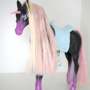 May include: Black unicorn toy with a light blue saddle and long, multi-colored hair. The unicorn has purple hooves and a pink horn.