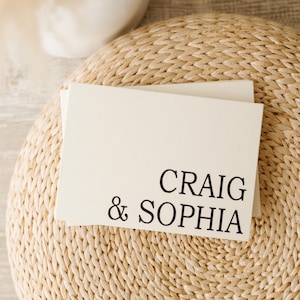 Puede incluir: Una tarjeta blanca con el texto "CRAIG & SOPHIA" sobre una estera de paja tejida.