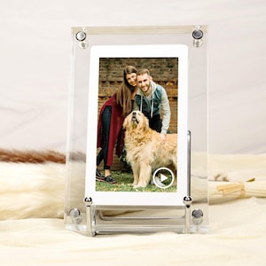 Könnte beinhalten: Transparenter Acryl-Fotorahmen mit einem Foto eines Paares und eines Golden Retrievers. Der Rahmen hat silberfarbene Beschläge und einen Ständer. Das Foto zeigt das lächelnde Paar mit dem Hund. Der Rahmen steht auf einer weißen Oberfläche.