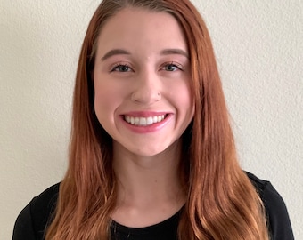 May include: A woman with long, wavy, auburn hair is smiling at the camera. She is wearing a black, long-sleeved shirt.