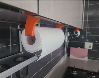 May include: Orange paper towel holder mounted under a cabinet with a roll of paper towels. The holder is made of plastic and has a simple design.