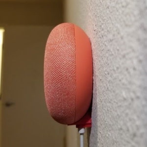 May include: A coral-coloured smart speaker mounted on a white wall. The speaker has a textured fabric covering.