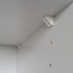 Op de afbeelding: Witte kastdeur met een wit kunststof scharnier. De deur heeft meerdere kleine gaten die erin zijn geboord.