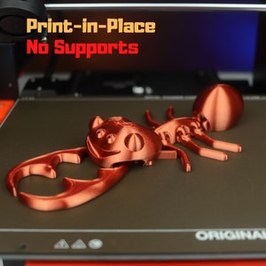 Può includere: Una statuetta di formica a forma di 3D stampata, di colore rame, con un viso sorridente. Il testo "Print-in-Place No Supports" è visibile sullo sfondo.