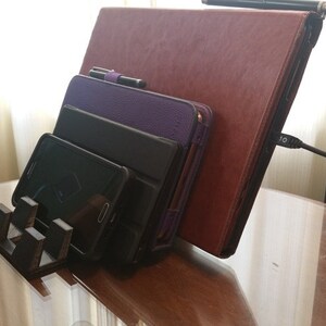 May include: A wooden stand holds a variety of devices, including a smartphone, a tablet, and a laptop. The stand is made of dark wood and has a simple design. The devices are all in different colours and sizes.