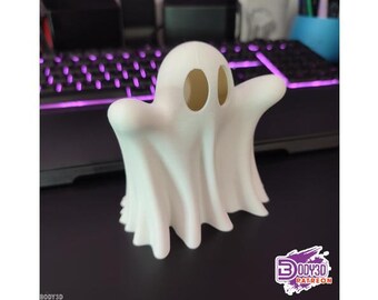May include: A white 3D printed ghost figurine with two round eyes. The ghost is standing on a dark surface.