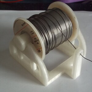 May include: A white plastic spool holder with a roll of silver solder wire. The spool is labeled "COORDINATED" and "0.032" in black text.