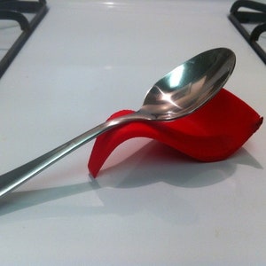 Puede incluir: Un reposacucharas de silicona rojo con una cuchara de plata apoyada encima.