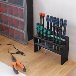 May include: A black plastic screwdriver holder with 18 screwdrivers. The screwdrivers have black handles with green and blue accents. The holder is on a wooden surface.