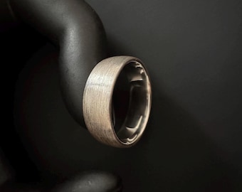 Könnte beinhalten: Ein Ring aus gebürstetem Metall mit strukturierter Oberfläche. Der Ring hat eine silberfarbene Außenseite und eine polierte Innenseite. Der Ring ist im Bandstil gehalten und für den täglichen Gebrauch geeignet.