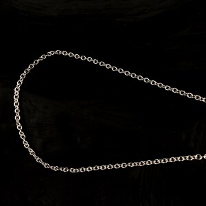 May include: A silver-colored chain necklace with small, circular links. The chain is displayed against a black background, highlighting its metallic sheen and delicate design. This necklace is suitable for everyday wear.