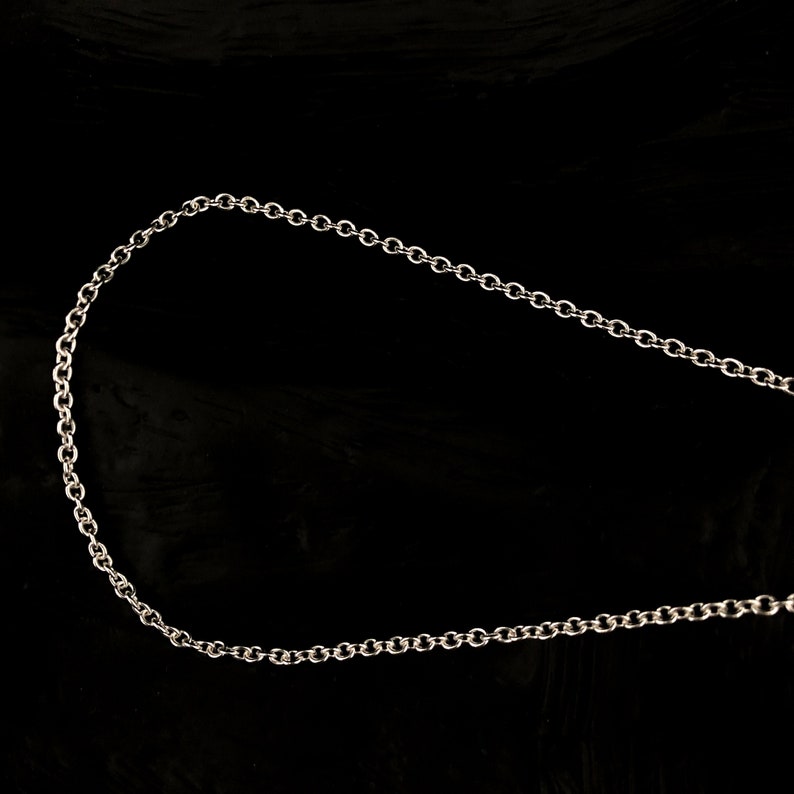 May include: A silver-colored chain necklace with small, circular links. The chain is displayed against a black background, highlighting its metallic sheen and delicate design. This necklace is suitable for everyday wear.