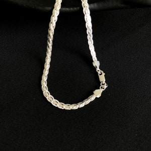 May include: A silver chain necklace with a woven pattern. The necklace features a lobster clasp fastening. The jewellery is shown against a black backdrop.