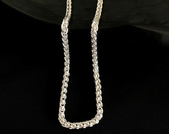 Op de afbeelding: Een zilverkleurige tarweketting met een doorlopend, ingewikkeld gevlochten schakelpatroon. De metalen schakels zijn hoogglanzend gepolijst, wat zorgt voor een uniforme, getextureerde uitstraling over de gehele lengte van de ketting.