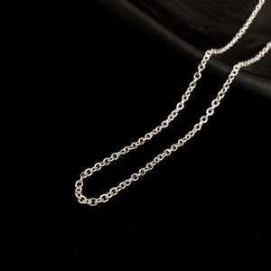 May include: A silver-colored chain necklace with small, round links. The chain is displayed against a black background, highlighting its reflective surface and delicate design. The necklace appears to be a simple, elegant piece of jewelry.