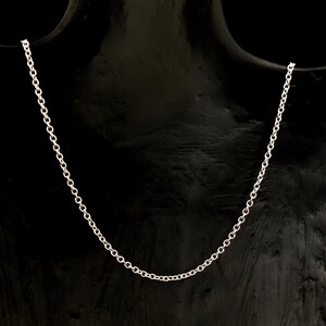 May include: A silver-colored chain necklace displayed on a black mannequin. The necklace is a delicate, simple design, with small, evenly spaced links. The chain is draped, showcasing its length and form. The background is a solid black.