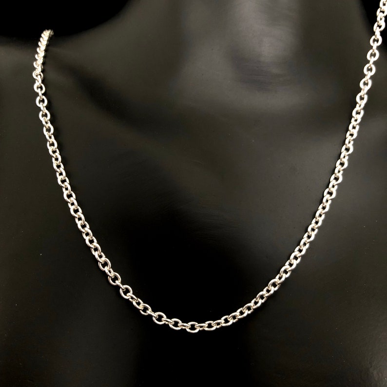 May include: A silver-colored chain necklace with a classic cable link design. The necklace is displayed on a black mannequin, showcasing the chain's polished finish and the individual links that make up the necklace.