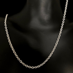 May include: A silver-colored chain necklace with a classic cable link design. The necklace is displayed on a black mannequin, showcasing its simple elegance. The chain is made of a shiny metal.