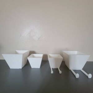 May include: Four white ceramic planters, three with legs, arranged in a row on a grey surface. The planters are different sizes, with the largest planter on the left and the smallest planter on the right.