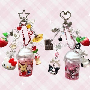 May include: Two keychains with pink drink-shaped charms, each adorned with various charms like strawberries, hearts, and character figures. One keychain has a star-shaped clasp, the other a heart. The charms include Hello Kitty and Kuromi characters.