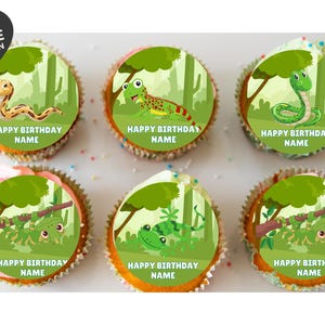 May include: Six cupcakes topped with circular edible toppers featuring jungle scenes with snakes, lizards, and geckos. Each topper includes the text HAPPY BIRTHDAY NAME in white capital letters. A black heart-shaped logo reads EDIBLE BY DESIGN.