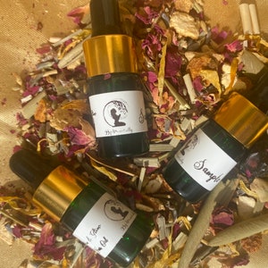Pode incluir: Tr&ecirc;s pequenos frascos de vidro com tampas douradas e etiquetas. Os frascos est&atilde;o cheios de um l&iacute;quido transparente e est&atilde;o sobre um leito de ervas e flores secas. Os r&oacute;tulos dos frascos dizem "Sample", "& Glow Oil" e "By Me Naturally".