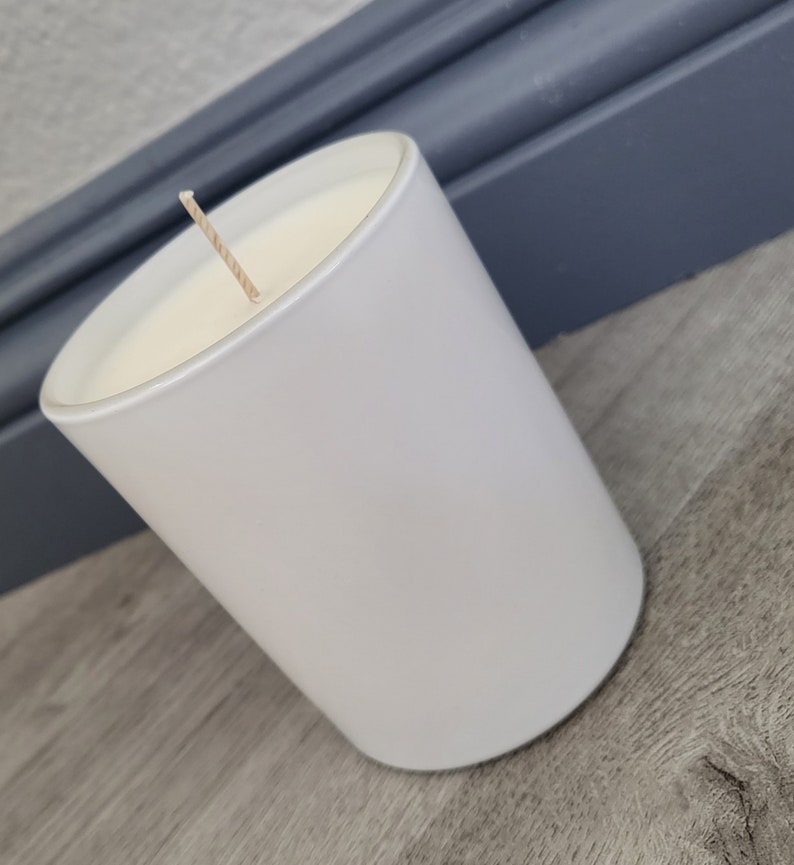 May include: A white candle in a white glass jar with a single wick.