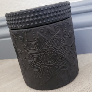 May include: Black ceramic candle jar with a floral design and a textured lid.