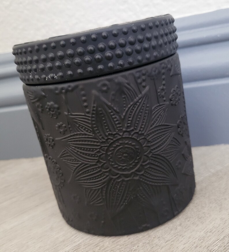 May include: Black ceramic candle jar with a floral design and a textured lid.