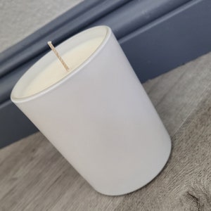 May include: A white candle in a white glass jar with a single wick.