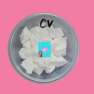 以下が含まれることがあります： 白い蓋が付いた透明なプラスチック容器に、白いチョークの塊が入っています。蓋には黒いマーカーで「CV」と書いてあります。
