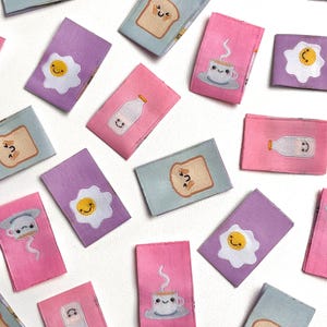 Op de afbeelding: Een verzameling van 15 kleurrijke stoffen patches met verschillende illustraties met een ontbijt-thema, waaronder een glimlachend ei, een kopje koffie, een glas melk en een snee toast. De patches zijn perfect om een ​​toets van whimsy toe te voegen aan knutselen, kleding of woonaccessoires.