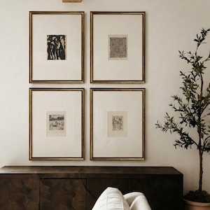 May include: Four rectangular framed art prints arranged in a grid on a wall. Each print features black ink illustrations on off-white paper, encased in thin gold frames with wide white matting. The artwork displays abstract and detailed line drawings.