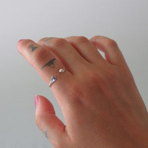 May include: A silver ring with a unique, hammered design. The ring is open and adjustable, making it a versatile piece of jewelry.