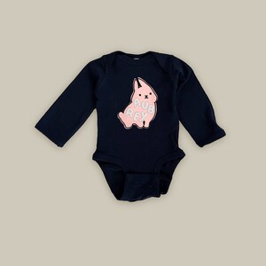 May include: A navy blue long-sleeved baby onesie with a pink bunny graphic and the text "Aubrey" on the front.