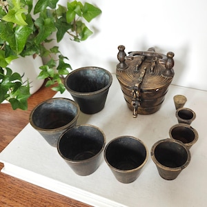 May include: A white ceramic mug with a black handle and the text "But First, Coffee" in a black, bold font. The mug is on a wooden surface. The mug is approximately 10 cm tall.