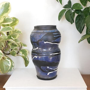 May include: A blue and black ceramic vase with a unique, abstract design. The vase has a rounded, bulbous shape and is decorated with black and white lines and swirls.