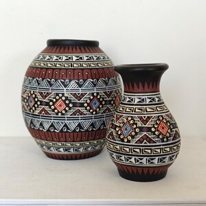 May include: Two rounded ceramic vases featuring a matte black base colour with intricate hand-painted geometric patterns in white, terracotta red, and blue. The designs include horizontal bands of triangles, diamonds, and linear motifs.