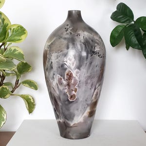 May include: A decorative vase with an abstract design. The vase has a blend of grey, white, and brown hues, creating a marbled effect. It has a rounded body and a narrow neck. The vase is approximately 46 cm tall.