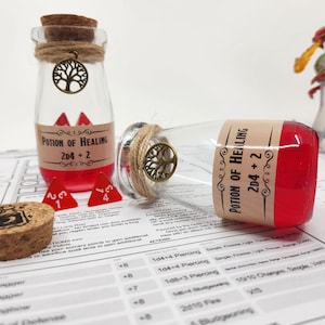 May include: Two glass bottles filled with red liquid and labelled "Potion of Healing 2D4+2". The bottles have cork stoppers and are decorated with twine and a small tree charm. Two red dice are in front of the bottles.