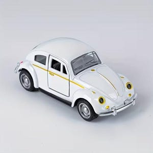 May include: A white die-cast toy car model of a classic beetle with a gold stripe running along the side. The vehicle features silver-coloured bumpers, circular headlights with yellow accents, and black wheels with silver hubcaps on a light background.