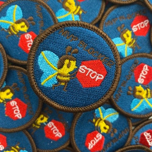 May include: A close-up of several embroidered patches featuring a cartoon bee holding a red stop sign. The patches are brown and blue with the text "My Relocker" on them.