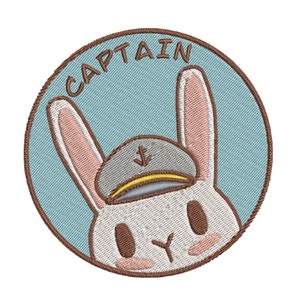 May include: A round embroidered patch with a blue background and the word "CAPTAIN" in brown stitching. A white rabbit with brown eyes and a gray sailor hat with a yellow band and an anchor is in the center of the patch.