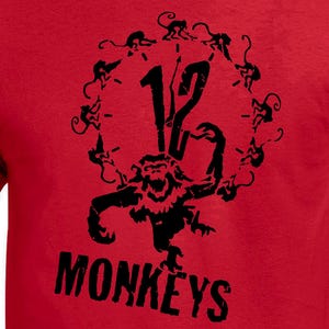 May include: Red t-shirt with a black graphic design. The design features the number 12 surrounded by a circle of monkey silhouettes, with a larger monkey figure below and the word "MONKEYS" in bold letters.