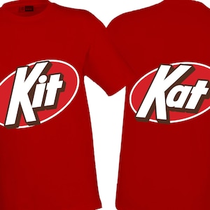 May include: Two red t-shirts with the Kit Kat logo printed on them. The logo is white text with a brown shadow inside a red oval with a white border. One shirt says "Kit" and the other says "Kat".