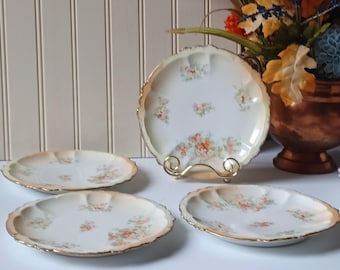 May include: Set of four antique porcelain plates with a floral design. The plates have a scalloped edge with gold trim and a cream-colored background. The floral pattern includes orange, pink, and green flowers.