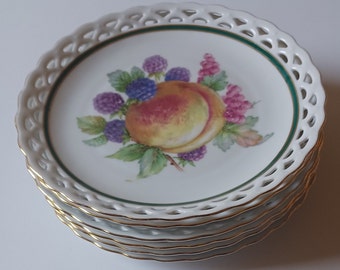 May include: A stack of six white ceramic dessert plates with a delicate lace-like edge and a gold rim. The center of each plate features a hand-painted design of a peach and blackberries.