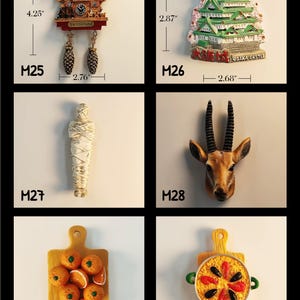 May include: A collection of decorative magnets. Includes a cuckoo clock (4.25" tall, 2.76" wide), Osaka Castle (2.87" tall, 2.68" wide), a mummy, a deer head, a cutting board with oranges, and a paella pan. Each magnet is labeled with a number.