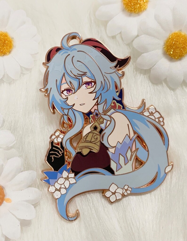 Op de afbeelding: Een gouden emaille pin met een personage met lang blauw haar, een rood-zwart hoofdband en een gouden bel. Het personage draagt een wit-blauwe outfit met een rood-gouden ontwerp. De pin is omringd door witte bloemen.